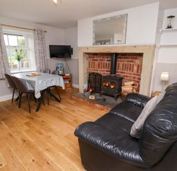 A living room with a fireplace, sofa, and dining table at Heather Cottages - Brent Goose in Bamburgh