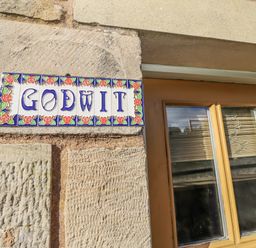 A sign labeled Godwit on a stone wall near a window at Heather Cottages - Godwit in Bamburgh