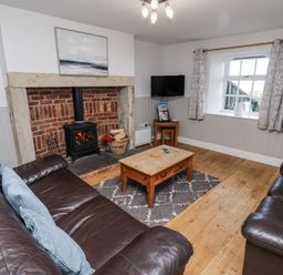 A living room with a wood stove and sofa at Heather Cottages - Godwit in Bamburgh