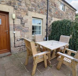 An outdoor seating area with a wooden table and chairs at Heather Cottages - Grayling in Bamburgh