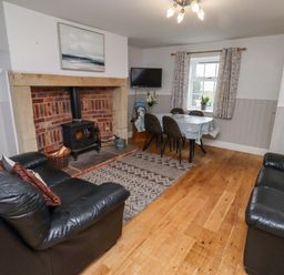 A living room with a fireplace and dining table at Heather Cottages - Grayling in Bamburgh