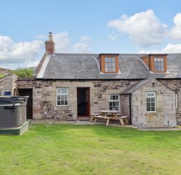 An outdoor view of a cottage with a hot tub and table at Heather Cottages - Grey Seal Bamburgh
