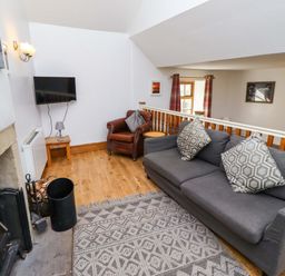 A living room with a sofa, armchair, and television at Heather Cottages - Grey Seal in Bamburgh