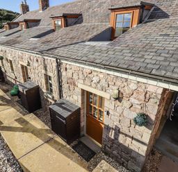 An outdoor view of a stone building with windows and pathways at Heather Cottages - Plover in Bamburgh