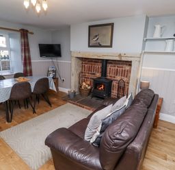 A living room with a sofa, dining table, and fireplace at Heather Cottages - Plover in Bamburgh