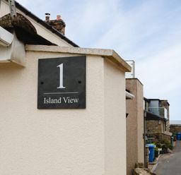 A street view showing a wall with a sign reading 1 Island View and buildings alongside a road at Island View in Amble