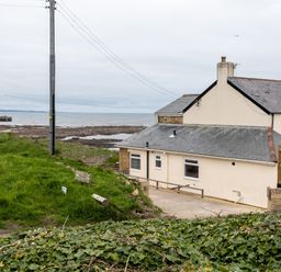 A house by the rocky shoreline with a grassy hill and power lines at Island View in Amble
