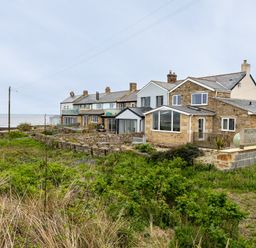 A row of stone and brick houses with glass extensions near the coast with vegetation in the foreground at Island View in Amble