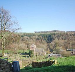 A rural landscape with a church and gravestones surrounded by fields and trees at Kirknowe in Jedburgh