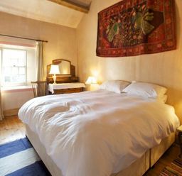 A bedroom with a large bed lamps a wooden dresser with mirror a chair and a window at Kirknowe in Jedburgh