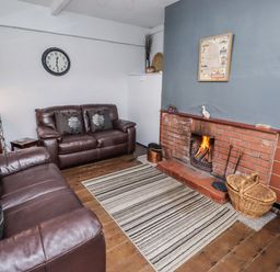 A living room with a fireplace and a sofa at Kittiwake Cottage, Budle Bay
