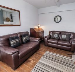 A living room with brown sofas and a mirror at Kittiwake Cottage, Budle Bay