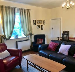 A living room with leather sofas a wooden coffee table curtains on the window and framed butterfly pictures on the wall at Leazes Cottage in Rothbury