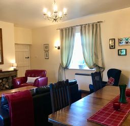 A living room with armchairs a wooden dining table with candles and a vase a fireplace and butterfly pictures on the wall at Leazes Cottage in Rothbury