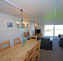 A dining table with wooden chairs and a living room with black sofas and a television near a large window at Longstone in Embleton