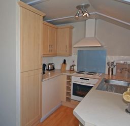 A kitchen with wooden cabinets a white oven stovetop and a sink with cups on the counter at Longstone in Embleton