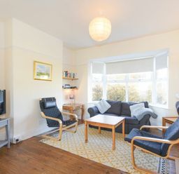 A living room with a sofa two armchairs a wooden coffee table a television on a stand and a large window at Melvin Cottage in Low Newton-By-The-Sea