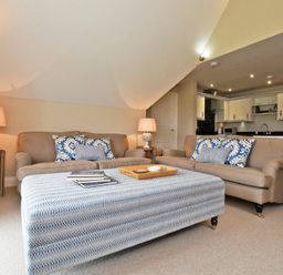 A living room with two sofas a large ottoman and a kitchen area at Sandpiper Bamburgh