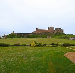 A large green lawn with a historic castle in the background and a partially visible house with a chair on the right side at Sandpiper Bamburgh