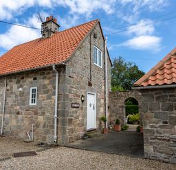 A stone house with a red tiled roof and a courtyard at Mid Cote in Shoreston near Bamburgh