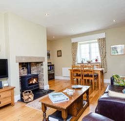 A living room with a wood stove fire television wooden furniture and a dining table at Mid Cote Shoreston near Bamburgh