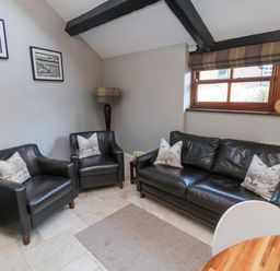 A seating area with two armchairs and a sofa with cushions a floor lamp and framed pictures on the wall at Nurses Cottage in Alnwick