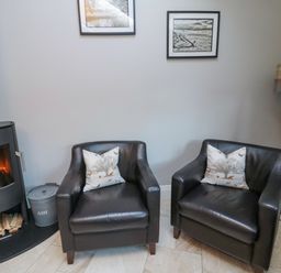 Two black leather armchairs with patterned cushions between a wood stove and a tall floor lamp in a sitting room at Nurses Cottage in Alnwick