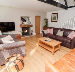A living room with sofas a coffee table a wall-mounted television a fireplace and stairs at Old Stable Cottage in Alnmouth