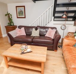 A living room with two sofas a wooden coffee table a floor lamp and stairs at Old Stable Cottage in Alnmouth