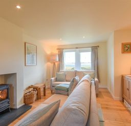 A living room with sofas a wood burning stove a lamp and a wooden cabinet at Ottoline Cottage in Embleton