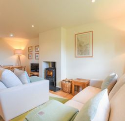 A living room with two sofas a wood-burning stove a basket with firewood lamps and a dining table at Ottoline Cottage in Embleton
