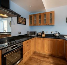A kitchen with wooden cabinets a black countertop an oven a microwave a kettle and a toaster at Pilots Rest in Alnmouth