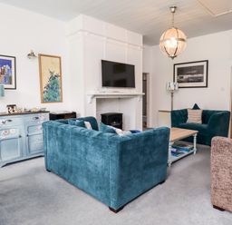 A living room with blue sofas a wooden coffee table and a TV above a fireplace at Salty Dog in Bamburgh