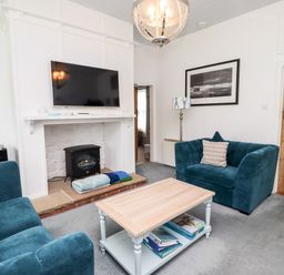 A living room with two blue armchairs a wooden door a fireplace with a TV above and a coffee table at Salty Dog in Bamburgh