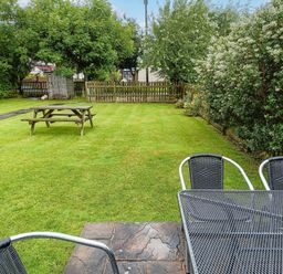A backyard with a picnic table on grass and metal outdoor chairs around a table at Salty Dog in Bamburgh