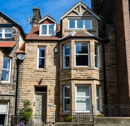 A stone house with bay windows and a green door between neighboring buildings at Upper Alnbank in Alnmouth