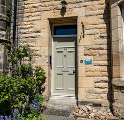 A front door with the number 14 on a stone building with plants and flowers at Upper Alnbank in Alnmouth