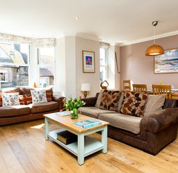 A living room with two sofas a coffee table with flowers and a dining table with chairs at Upper Alnbank in Alnmouth