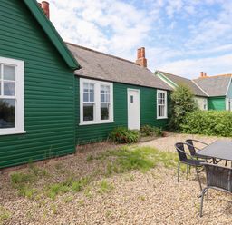 A gravel yard with outdoor table and chairs next to green wooden cottages at Sand Dune Cottage in Bamburgh