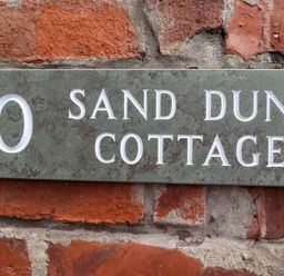 A house number plaque mounted on a brick wall at Sand Dune Cottage in Bamburgh