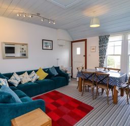 A living room with a blue sectional sofa and dining table with chairs at Sand Dune Cottage in Bamburgh