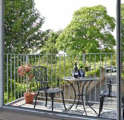 A balcony with two chairs a round table with wine and glasses and a potted plant at Schooner Court No1 in Alnmouth