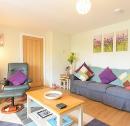 A living room with a grey sofa and colorful cushions a green armchair a wooden coffee table and a bookshelf at Schooner Court No2 in Alnmouth