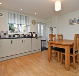 A kitchen with wooden dining table and chairs next to gray cabinets and a window at Schooner Court No2 in Alnmouth