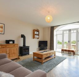 A living room with a wooden coffee table a wood stove a TV and large arched windows at Sea Breeze in Newton-by-the-Sea