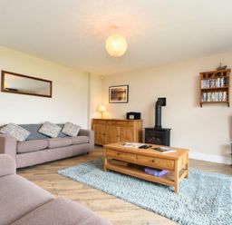 A living room with two sofas a wooden coffee table a wood burning stove and a television at Sea Breeze in Newton-by-the-Sea