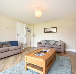 A living room with two sofas a wooden coffee table a floor lamp and a sideboard at Sea Breeze in Newton-by-the-Sea