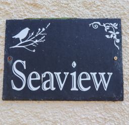 A black sign with the word Seaview and white bird and branch decorations on a textured beige wall at Seaview Howick Craster