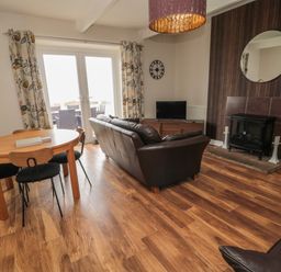A living room with a dining table and chairs a sofa a television and a fireplace at Seaview Howick in Craster