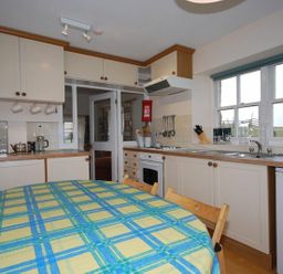 A kitchen with white cabinets, a round table with a yellow and blue checkered tablecloth, and a window at Snook Point Cottage in Newton-by-the-Sea
